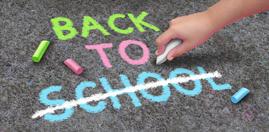 A student has written BACK TO SCHOOL in chalk on the concrete.  SCHOOL has been crossed out, to indicate there is more time off school due to teacher strikes.