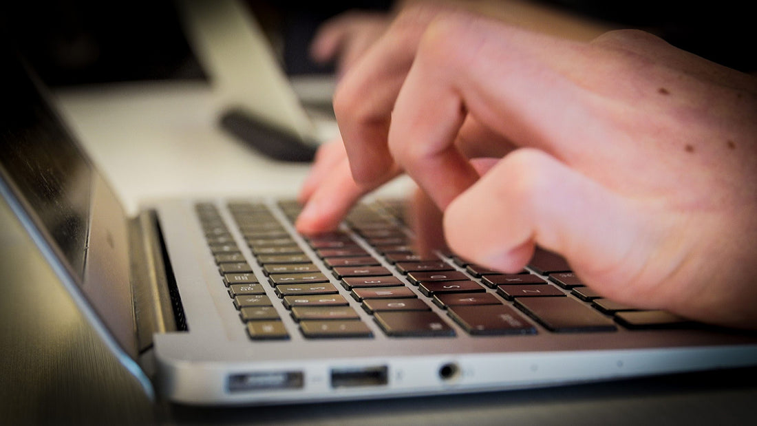 Hands are over a laptop's keyboard, typing.