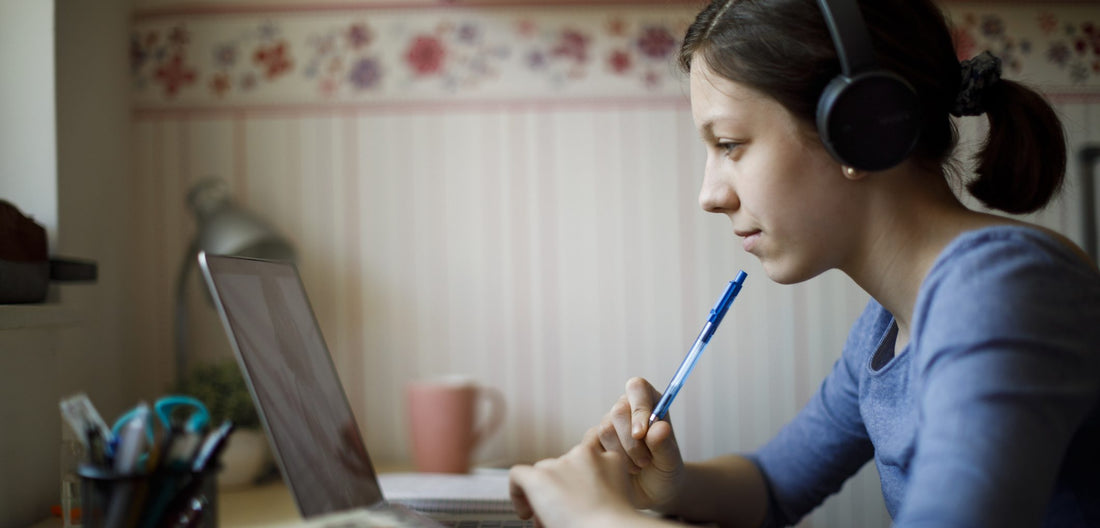 Girl sits at laptop for online learning and rests her pen on her chin