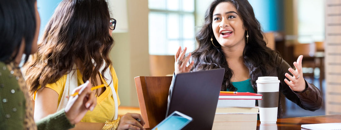 Teachers discuss things at a table, with devices open.